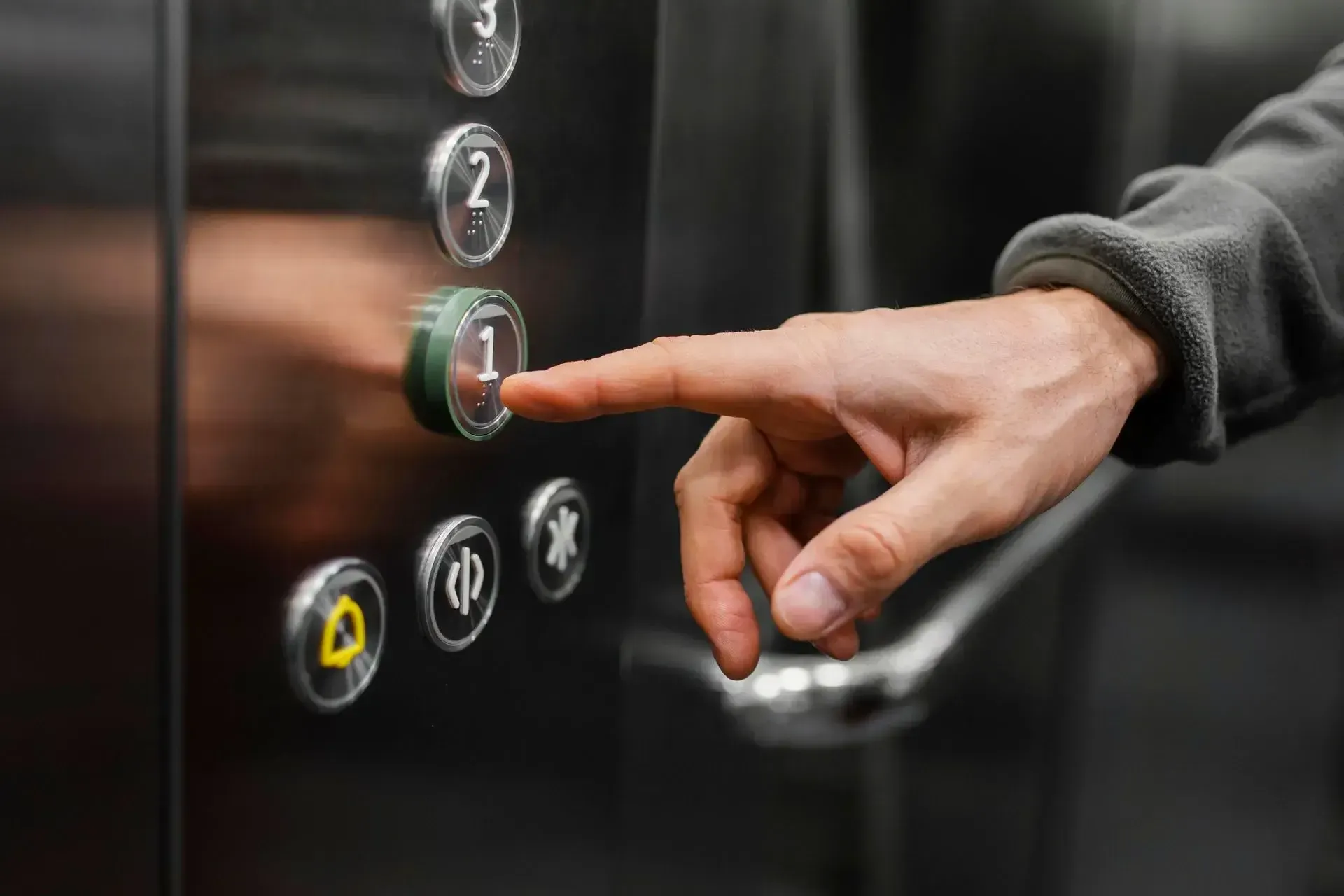 Inside a shiny, modern elevator, a person presses the button for the first floor. The control panel, featuring buttons marked with numbers, a door open button, a door close button, and emergency symbols, reflects recent updates provided by top-notch elevator repair services.