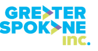 The image displays the logo for Greater Spokane Inc. The text "Greater Spokane" is written in blue with green and purple triangular arrows embedded within, arranged vertically. The word "inc." appears in green below "Spokane" on the right side.
