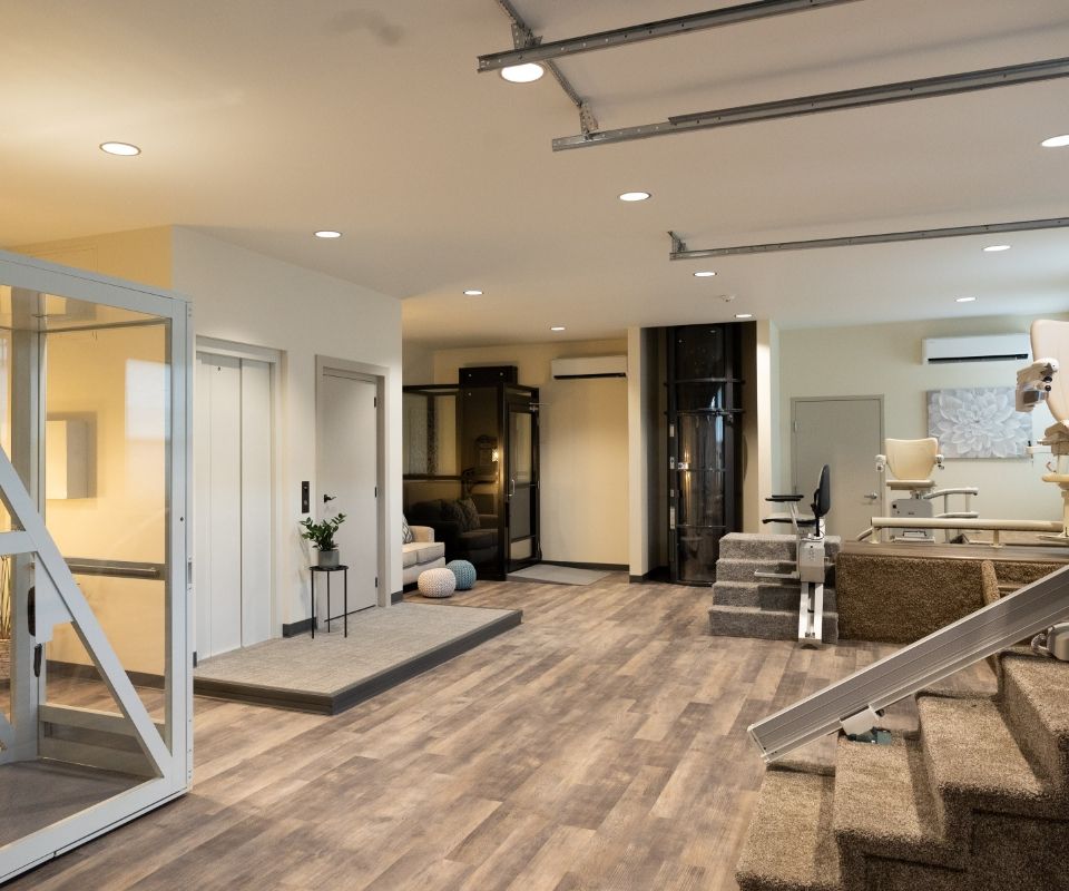 A modern interior showroom displays various home elevator models. The room has wooden floors, warm lighting, and multiple stair configurations leading to different elevators, showcasing accessibility options. The space is organized and well-lit, demonstrating the excellence in elevator service offered by top-tier contractors.